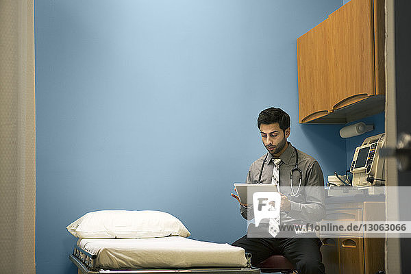 Arzt benutzt Tablet-Computer  während er im Krankenhaus auf einem Stuhl sitzt
