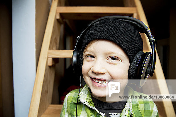 Porträt eines glücklichen Jungen  der zu Hause gegen eine Leiter Musik hört