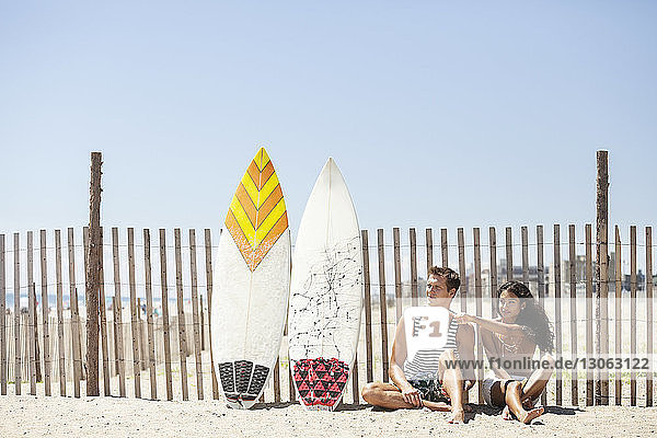 Woman pointing while sitting with boyfriend on sand against fence
