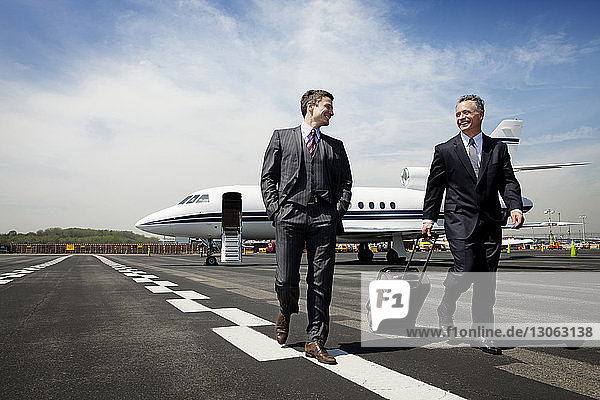 Happy businessmen walking on airport runway against sky