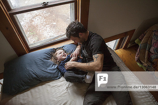 Hochwinkelansicht von Vater und Sohn beim Spielen  während sie zu Hause auf dem Bett liegen