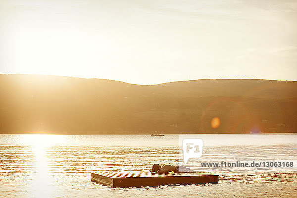 Junge liegt bei Sonnenuntergang auf schwimmender Plattform im See