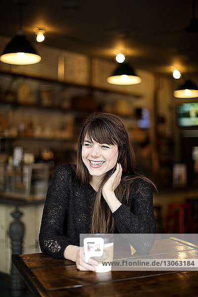 Lächelnde Frau mit Kaffee in der Hand und am Tisch im Café sitzend