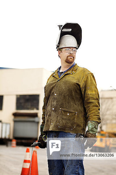 Nachdenklicher männlicher Arbeiter  der eine Schweißmaske trägt und in einer Recycling-Anlage steht