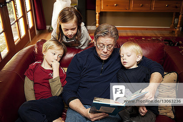 Hochwinkelansicht eines Großvaters  der Kindern Geschichten erzählt  während er zu Hause auf dem Sofa sitzt