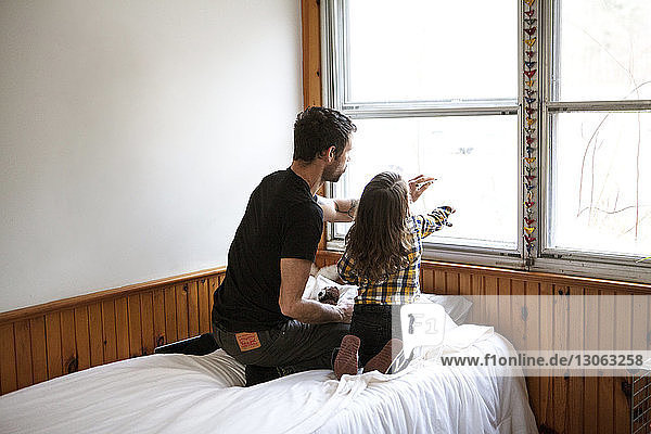 Rear view of father and son drawing on window glass while kneeling on bed