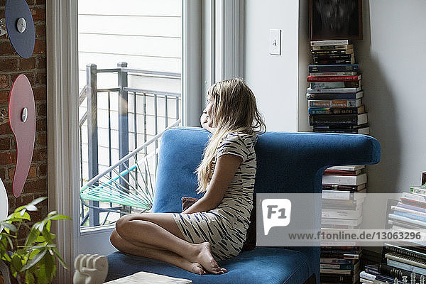 Woman looking through window while sitting on sofa at home
