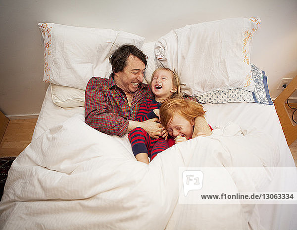 Father playing with sons while lying on bed at home
