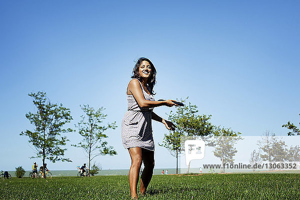 Verspielte Frau wirft Plastikscheibe  während sie im Park steht