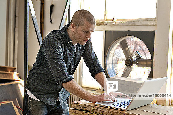 Seitenansicht eines männlichen Tischlers mit Laptop in der Werkstatt