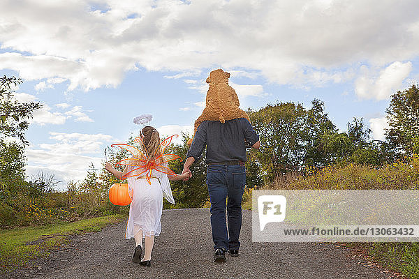 Rear view of father with children in Halloween costume walking on field