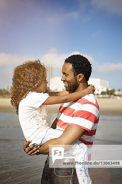 Mann trägt Tochter  während er am Strand gegen den Himmel steht