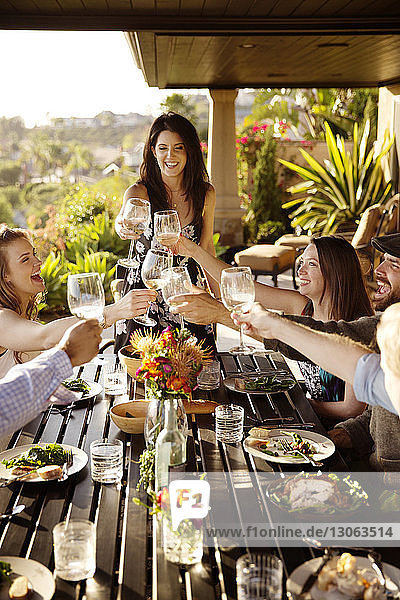 Glückliche Freunde stoßen am Esstisch auf der Veranda auf Weingläser an