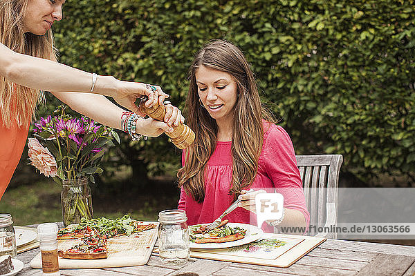 Frau mahlt Pfeffer auf Essen für einen Freund  während sie im Rasen am Tisch sitzt