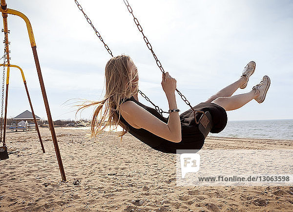 Side view of woman playing on swing against sky