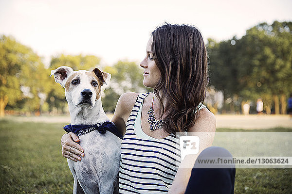 Loving woman sitting with dog on grassy field at park