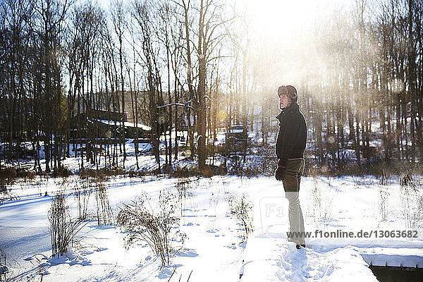 Man looking away while standing on snow covered field