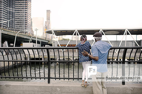 Rear view of grandfather and granddaughter standing at railing in city
