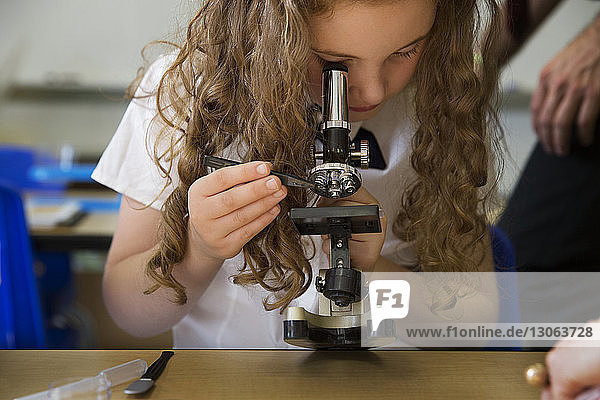 Girl looking through microscope while performing science experiment in laboratory