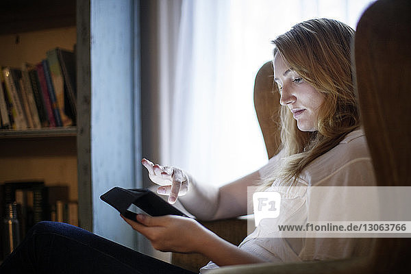 Frau benutzt Tablet-Computer  während sie zu Hause auf einem Sessel sitzt