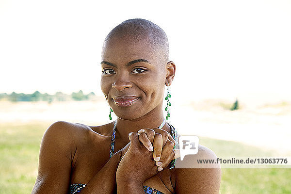 Portrait of happy shaved head woman standing with hands clasped on sunny day