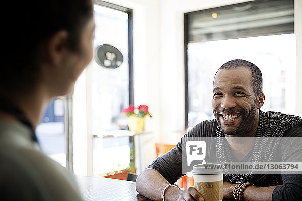 Glücklicher Mann hält Tasse und spricht mit dem Besitzer im Café