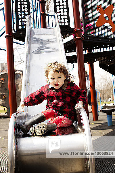 Porträt eines niedlichen Mädchens  das auf einer Rutsche auf einem Spielplatz sitzt