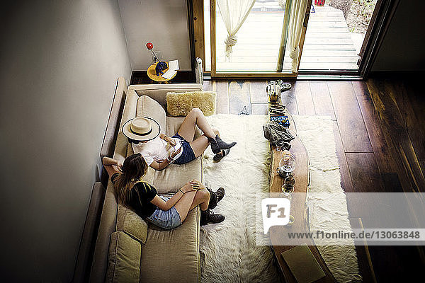 Hochwinkelansicht von Freunden  die ein Mobiltelefon benutzen  während sie zu Hause auf dem Sofa sitzen