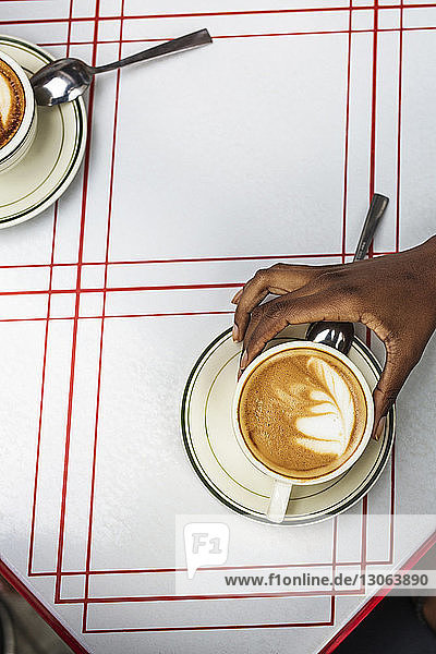 Ausschnitt eines Cappuccino in der Hand haltenden Cafes auf dem Bürgersteig
