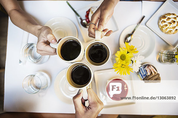 Cropped image of friends toasting with coffee cups at table in restaurant