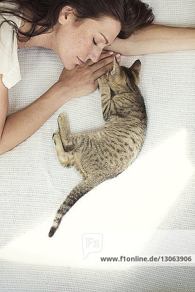 Hochwinkelansicht einer Frau  die zu Hause mit einer Katze auf dem Bett schläft