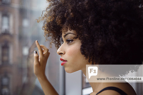 Nahaufnahme einer nachdenklichen Frau mit lockigem Haar  die durch ein Fenster schaut