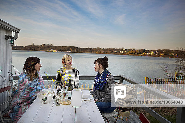 Friends talking while having food at porch against lake during winter
