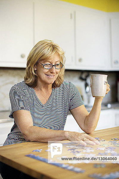 Frau hält Tasse beim Puzzlespielen zu Hause