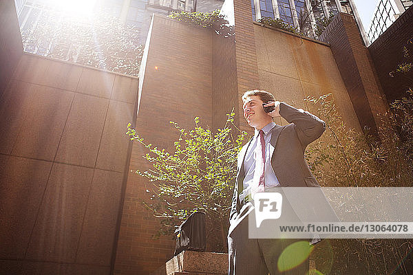 Niedriger Blickwinkel eines Geschäftsmannes  der mit einem Smartphone spricht  während er sich gegen Gebäude in der Stadt stellt