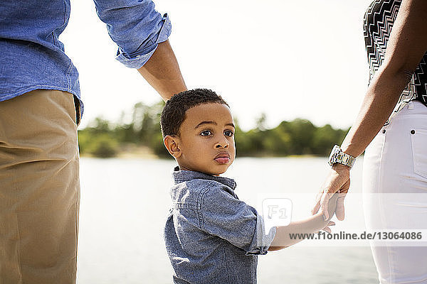 Boy looking away while standing with parents at lakeshore
