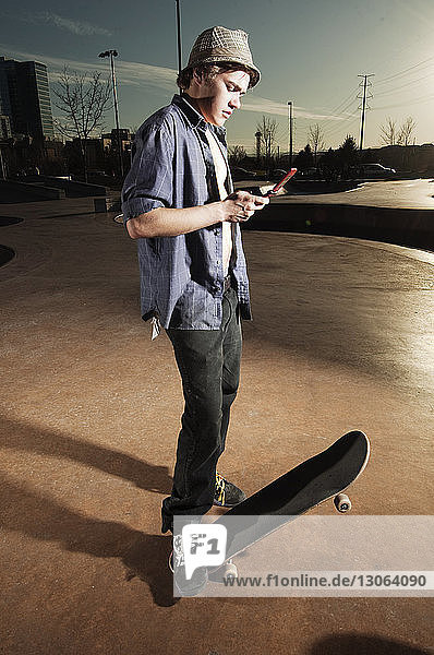 Mann benutzt Mobiltelefon  während er mit Skateboard auf der Sportrampe steht