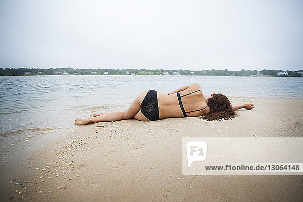 Rückansicht einer am Strand im Sand liegenden Frau