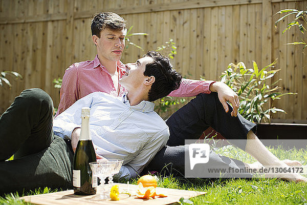 Gay men looking at each other while relaxing on field in backyard