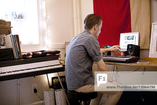 Side view of man with piano using laptop computer