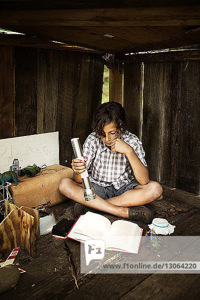 Junge hält Blitzlicht beim Lesen eines Buches im Baumhaus