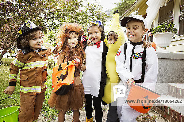 Fröhliche Kinder in Halloween-Kostümen  die während eines Streichs oder einer Behandlung im Hof stehen