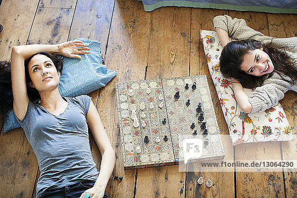 Sisters lying down by chess board at home