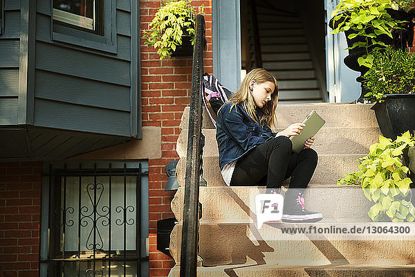Mädchen benutzt Tablet-Computer  während sie auf Stufen vor dem Haus sitzt