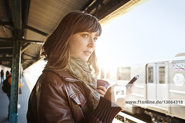 Frau schaut weg  während sie am Bahnhof ein Smartphone benutzt