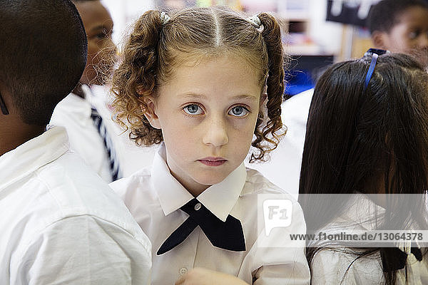 Portrait of schoolgirl standing with classmates in classroom