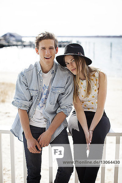 Porträt eines Paares  das auf einem Geländer am Pier vor dem Strand sitzt