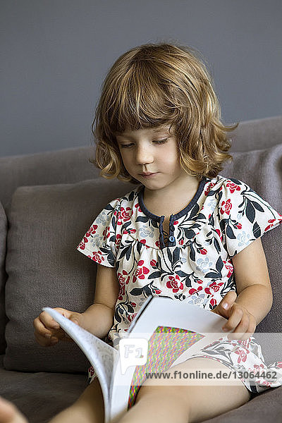 Mädchen hält Buch  während sie zu Hause auf dem Sofa sitzt