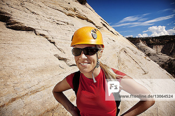 Lächelnde Frau mit Helm  die an einem sonnigen Tag vor einer Felsformation steht