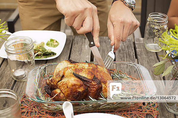 Cropped image of man carving roasted chicken at wooden table